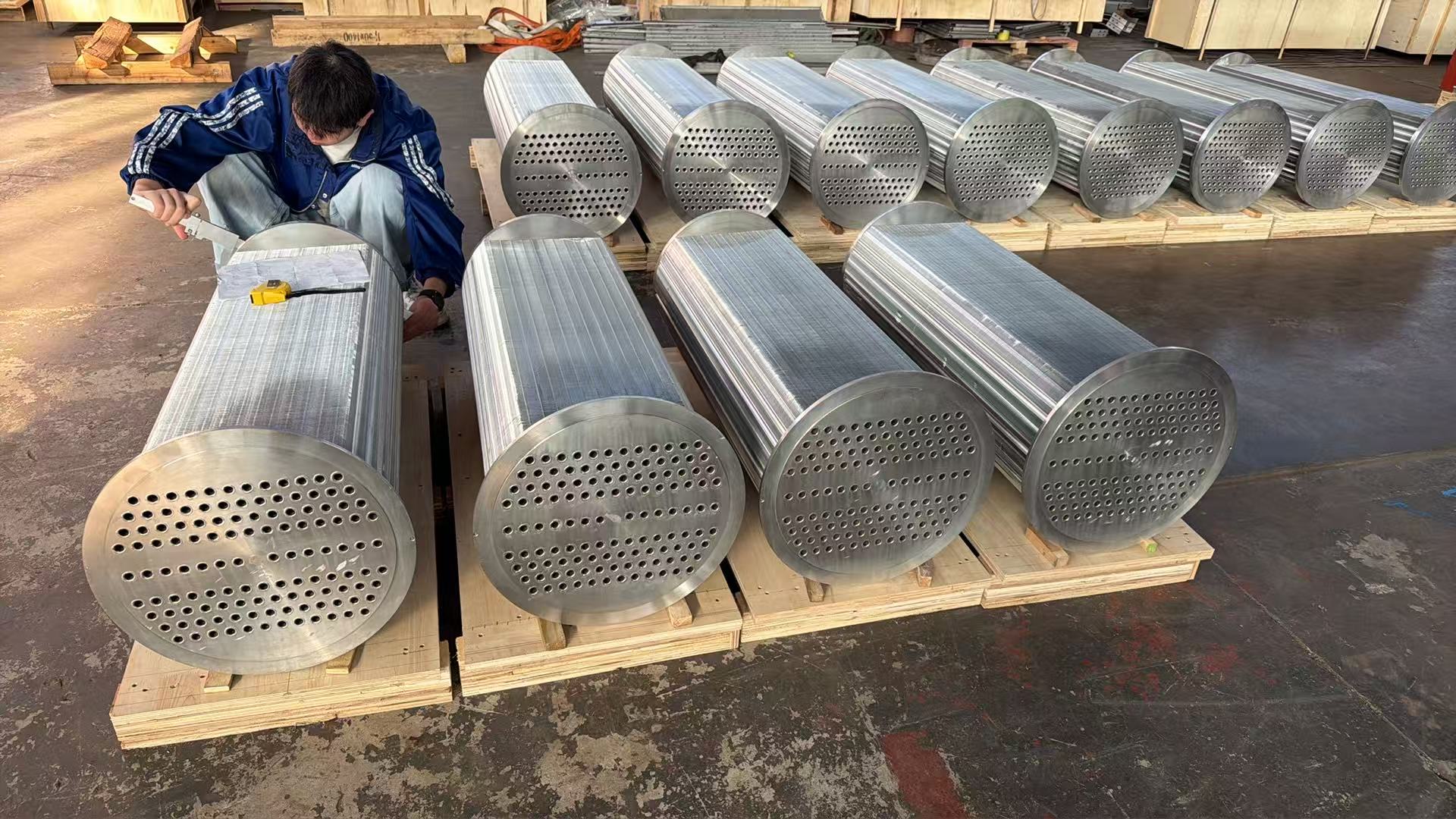 Atlas Copco ZH560 intercooler and aftercooler bundles on wooden crates at Turbomax Suzhou, technician using a steel tape measure to verify overall bundle length against the OEM drawing specification before final pressure testing