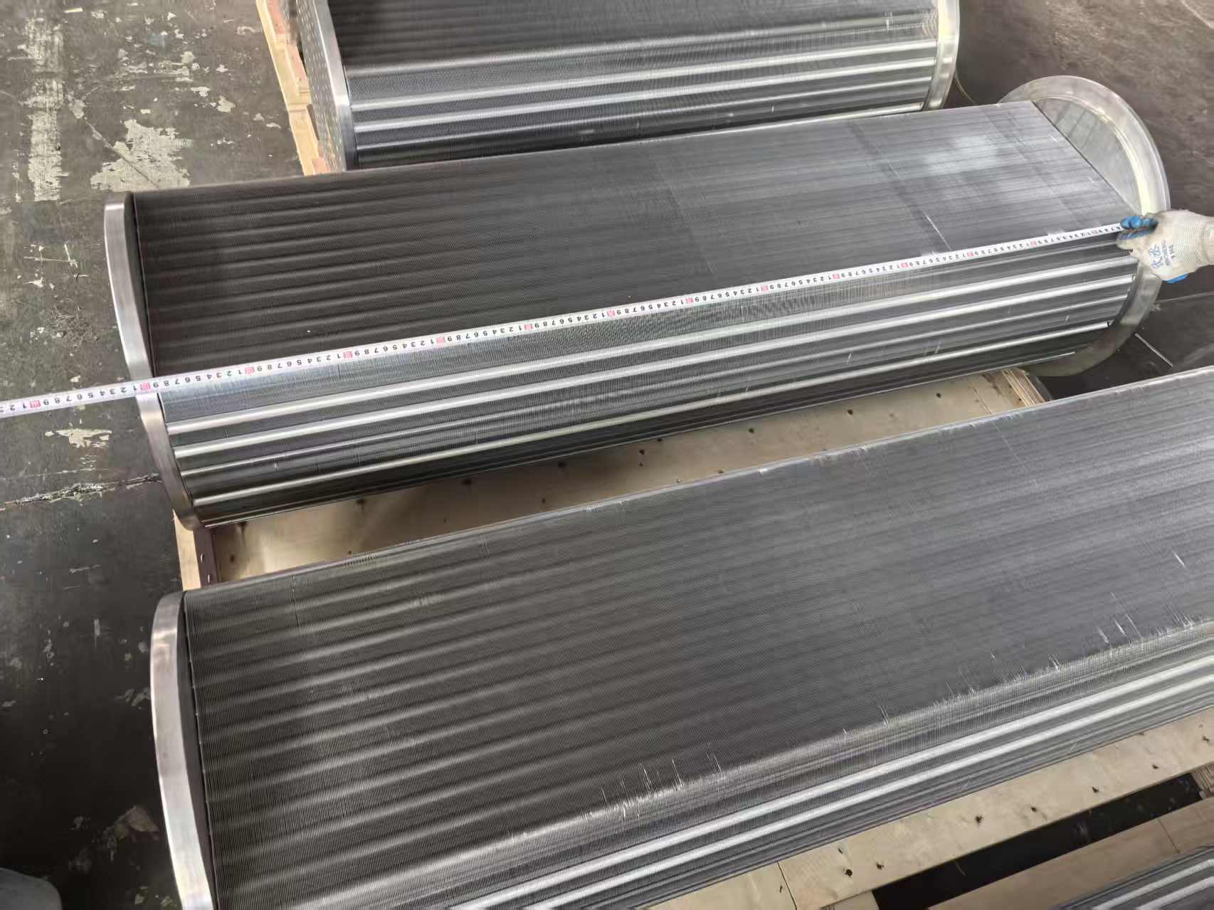 Close-up of technician's hand holding a steel ruler against an Atlas Copco ZH560 aftercooler bundle end, measuring tube sheet flatness and tube pitch as part of final QC inspection